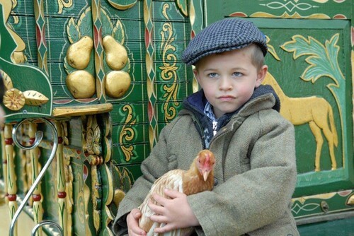 Boy holding Chicken in front of Romany Gypsy wagon wearing blue cap and green jacket