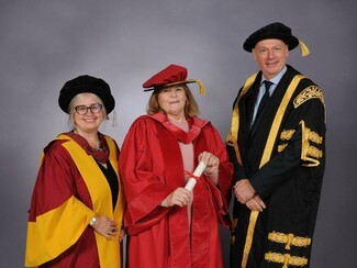 Three people in gowns and mortar boards recieving awards