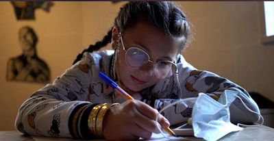 Girl sat at table writing with covid mask