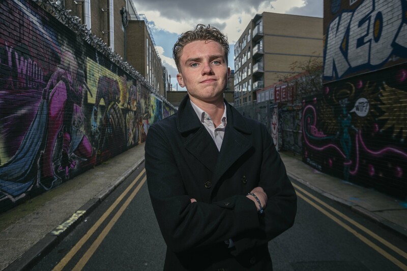 Jimmy Doherty stands with arms crossed, smiling, on a road with graffiti walls.