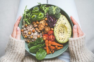 a pair of arms holding a bowl of vegetarian food