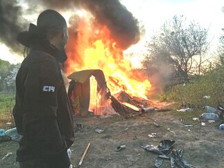 A Combat 14 Ukrainian neo-Nazi gang member looks on as a Roma camp burns 