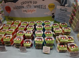 A sign shows green grass and a blue sky , in front of it sits various Grown Up Wagon Wheels with signs in front of them, denoting their flavours