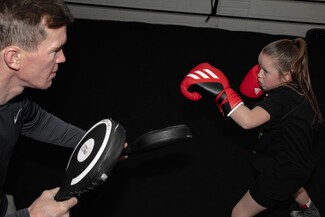 White male left holding boxing pads. white young female right wearing red boxing gloves training