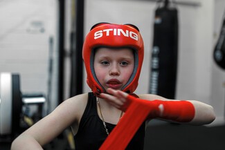 young white female wearing a red sparring helmet and wrapping her hand in red tape