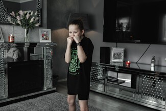 Young girl with brown pony tail with her fists up by her face, in her living room