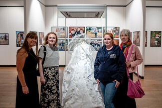 Leeds GATE staff and Cath Muldowney alongside one of the community member objects - a beautiful christening dress - featured in the exhibition