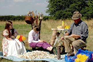 Young girls being showed how to create wooden flowers by a man 