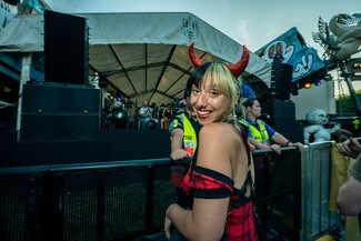 young white woman smile wearing balck and red dress and devil horn headband in front of a stage and speakers.